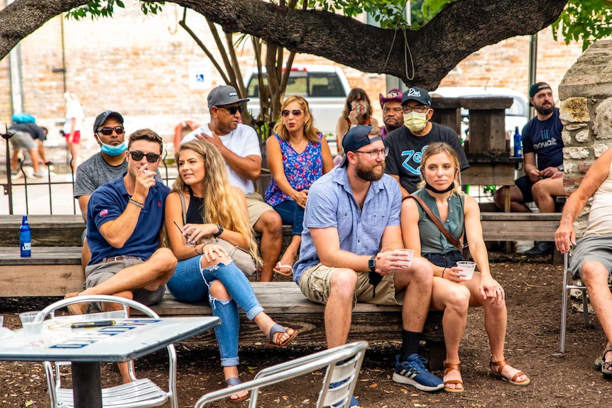 A group of young people sitting on benches in a beer garden with drinks in their hands