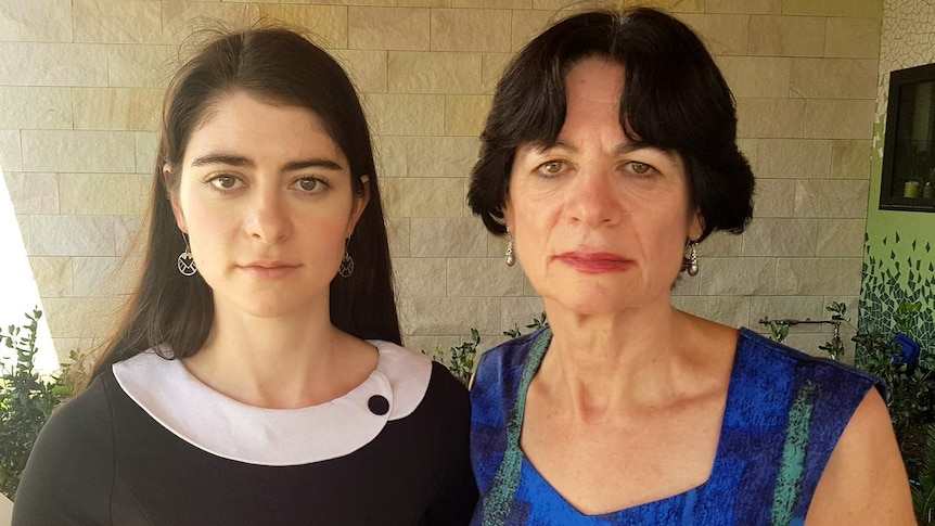 Two women stare ahead and do not smile
