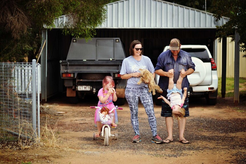 Playful parents stand in driveway with dog and two children.
