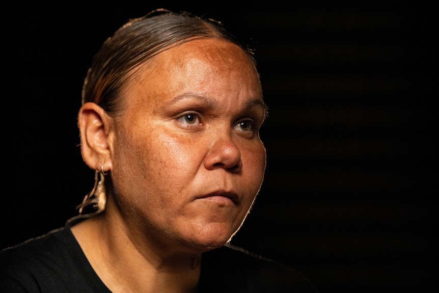 A head shot of an Indigenous lady with a serious expression pictured against a dark background