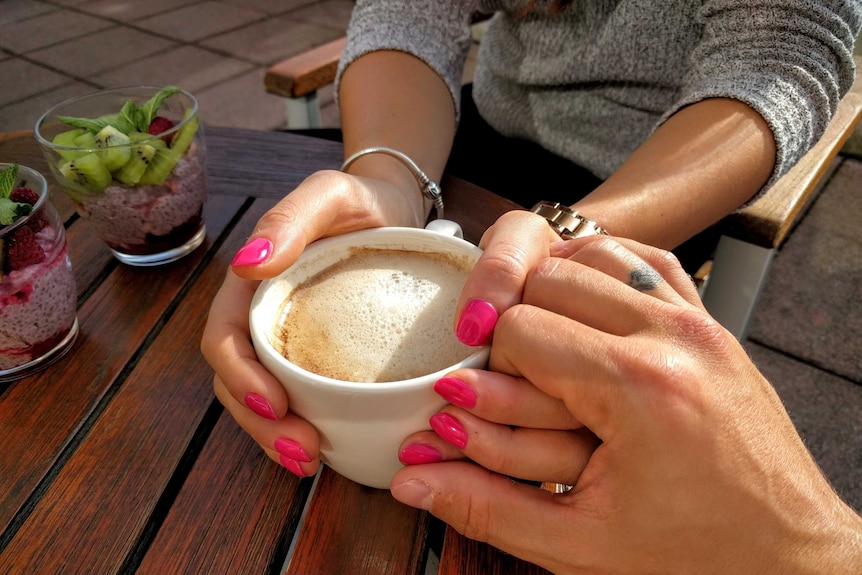 Close up of man holding the hand of woman holding a cup of coffee
