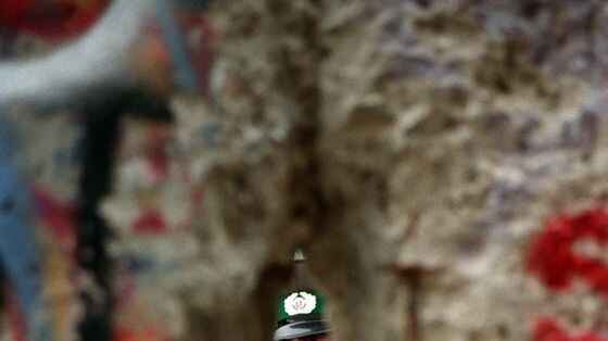 An East German policeman looks through a hole made in the Berlin Wall