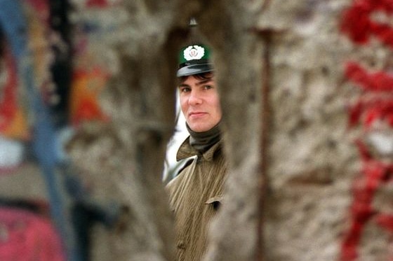 An East German policeman looks through a hole made in the Berlin Wall