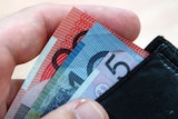 A person's hand takes Australian currency out of a wallet.