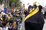 A man in a large Richmond-coloured balloon suit walks down the middle of the grand final parade.