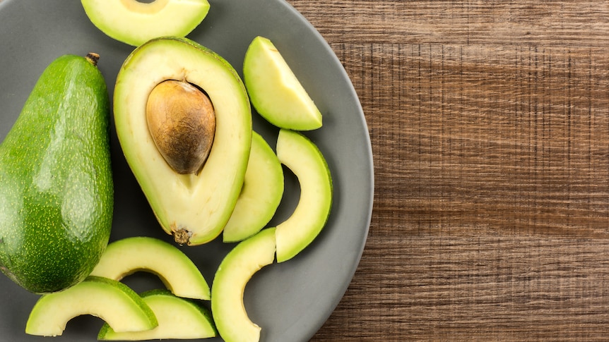 A whole, halved and sliced Shepard avocado, one variety commonly available in Australia.