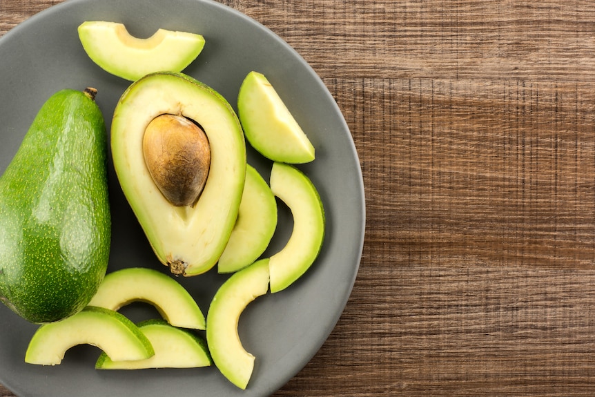 A whole, halved and sliced Shepard avocado, one variety commonly available in Australia.