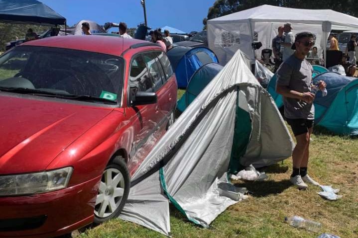 A red car is seen with its wheel over a damaged tent at Falls Festival.