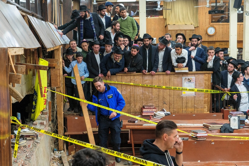 Bir sinagogun duvarındaki büyük bir deliğin önünde polis bandı var.  Bir grup Yahudi erkek, müfettiş hasarı inceliyor