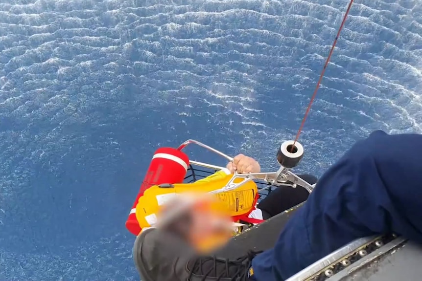 Paramedics lower down a rescue basket to get men out of the ocean.