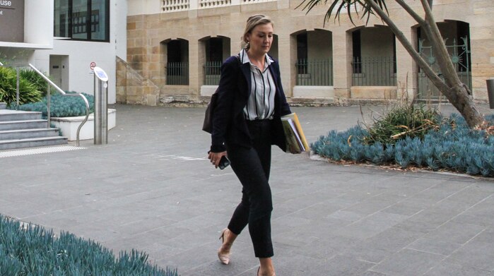 A slender woman in business attire walks across the courtyard in a court complex.