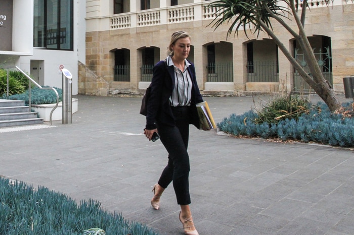 A slender woman in business attire walks across the courtyard in a court complex.