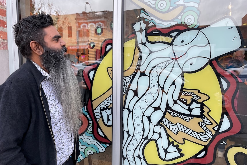 A man with a long beard looks at a graphic of a platypus. 
