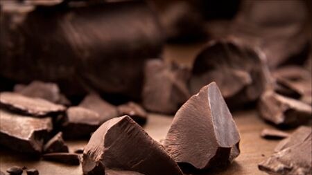 A chunk of dark chocolate sitting on a wooden chopping board.