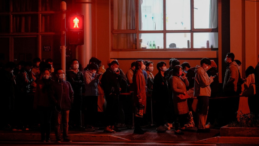People line up near a nucleic acid testing site outside a hospital at night.