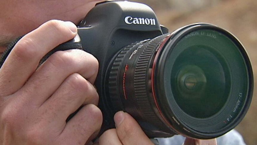A photographer looks through the lens of a camera.