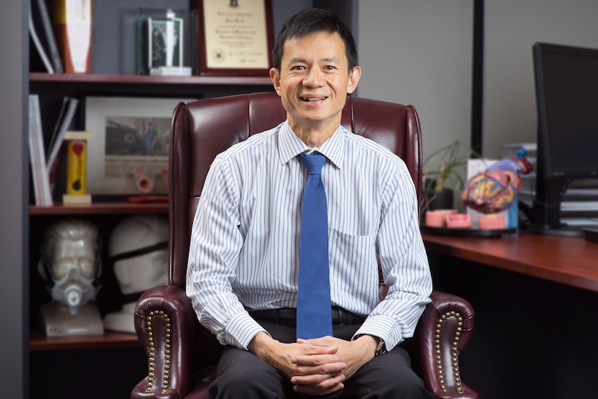 Dr Lim wears a shirt and tie and sits in an office, smiling at the camera