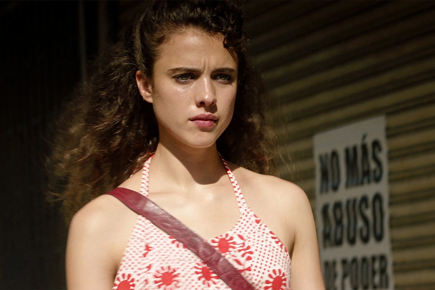 A 20-something woman with curly brown hair, wearing a sundress, looks concerned