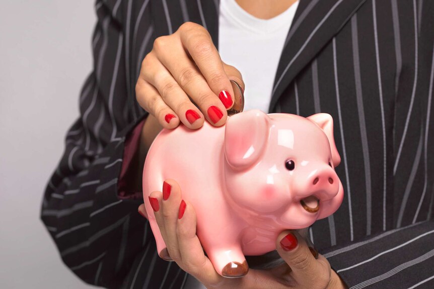 Woman wearing a striped jacket and a white top places a coin into the top of a piggy bank.