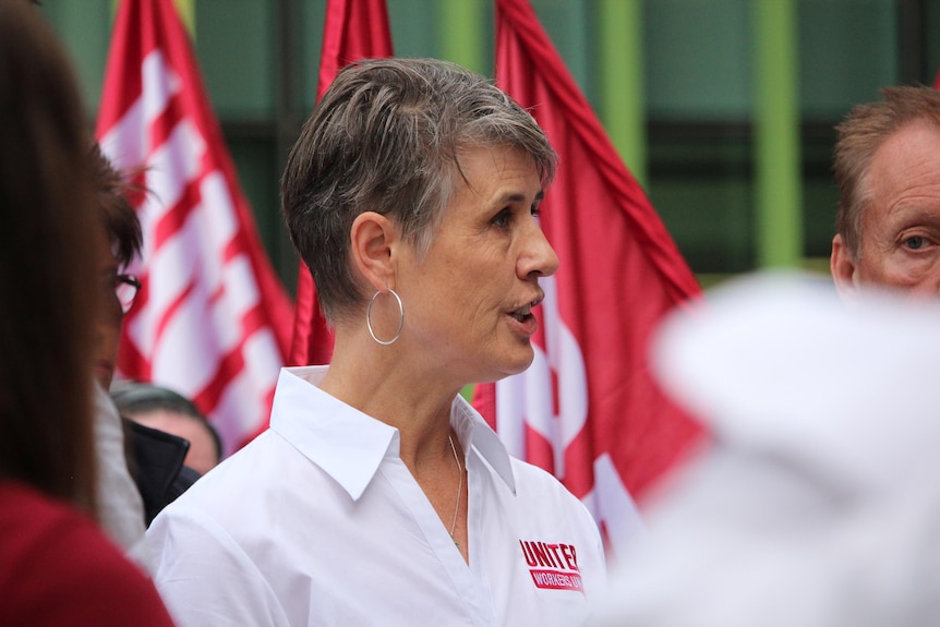 Carolyn Smith speaking in front of some red flags.