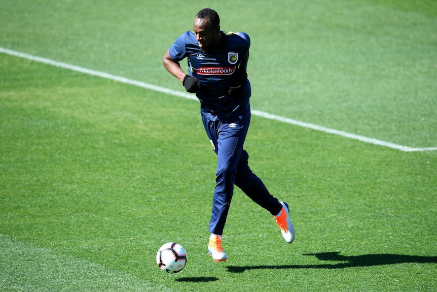 A footballer wearing a t-shirt and gloves runs with the ball