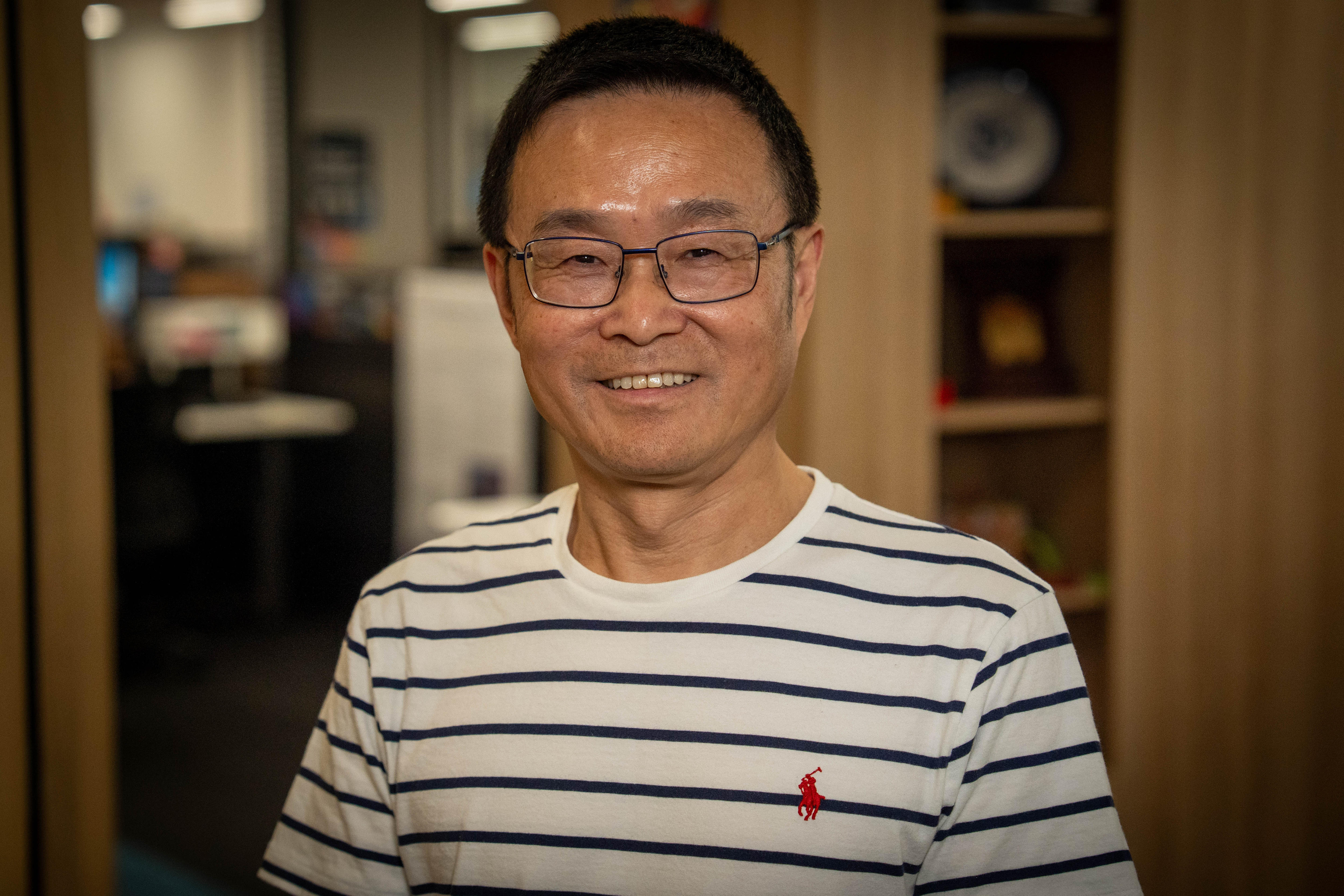 Un hombre sonríe a la cámara con un top a rayas y gafas.