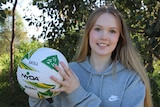 A teenage girl smiles as she holds a netball.