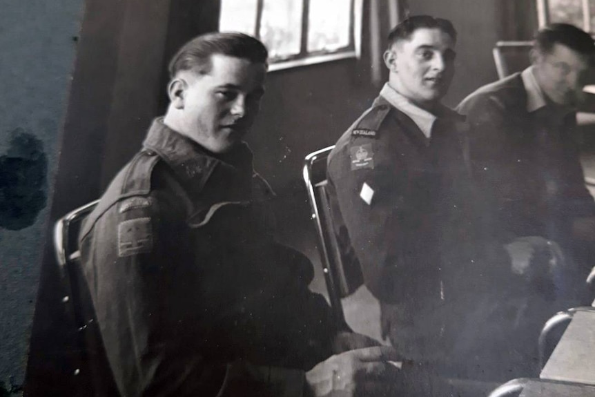 Black and white photograph of three service men in uniform sitting next to each other at a table 
