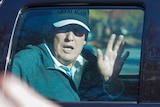 US President Donald Trump wearing a cap and waving from his motorcade.