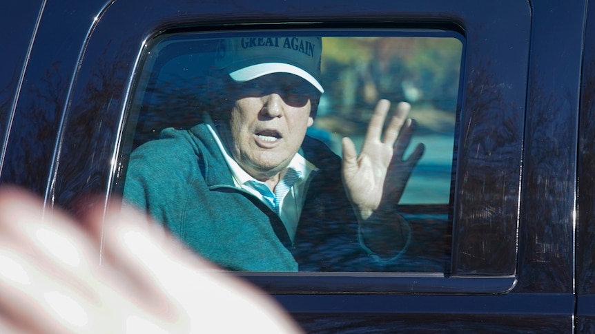 US President Donald Trump wearing a cap and waving from his motorcade.