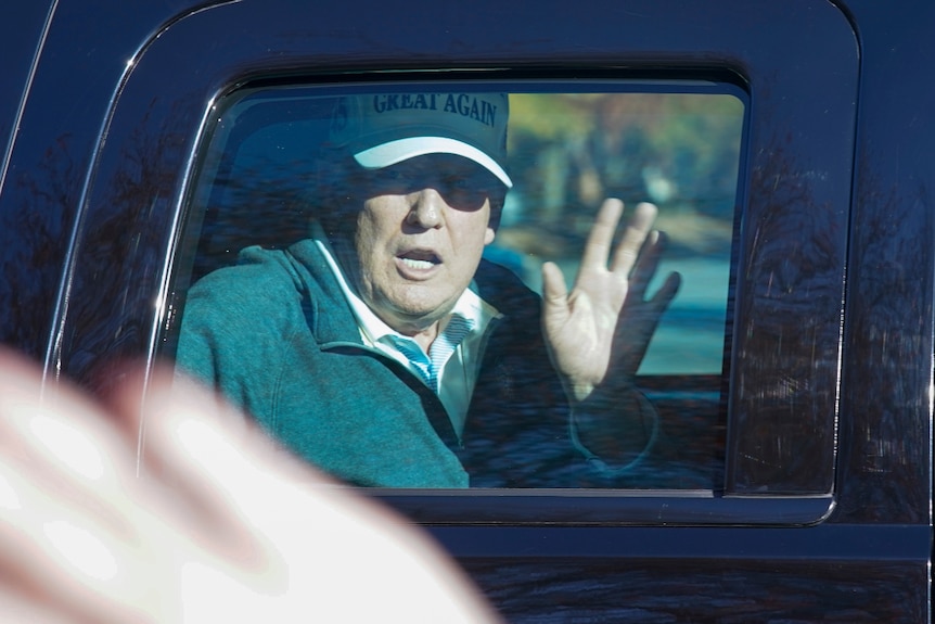 US President Donald Trump wearing a cap and waving from his motorcade.