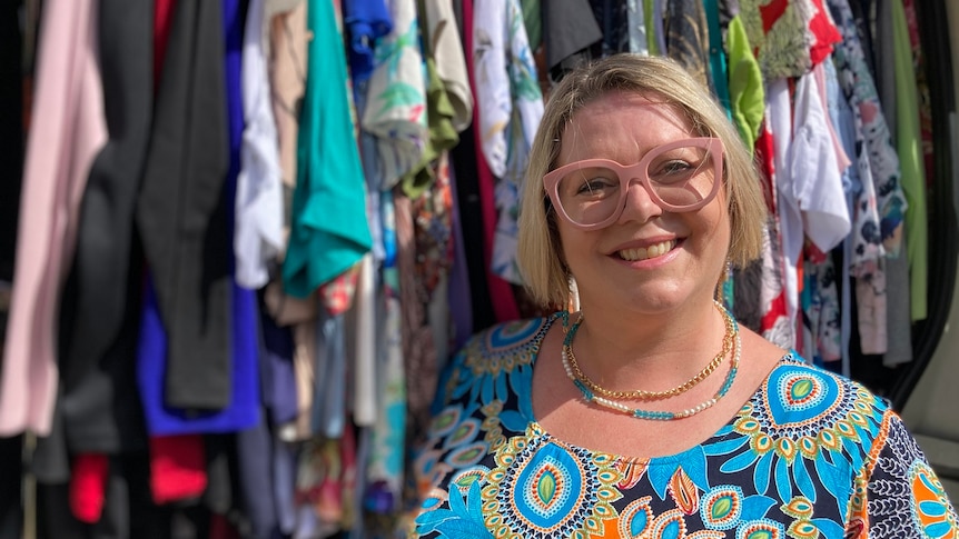 Michelle Darby smiles as she stands beside a rack of clothes at her mobile fashion boutique.