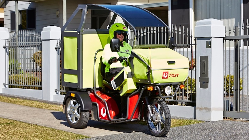 A postie clad in fluoro yellow clothes rides a motorised three wheeled motorbike which has a sunshade over the top.