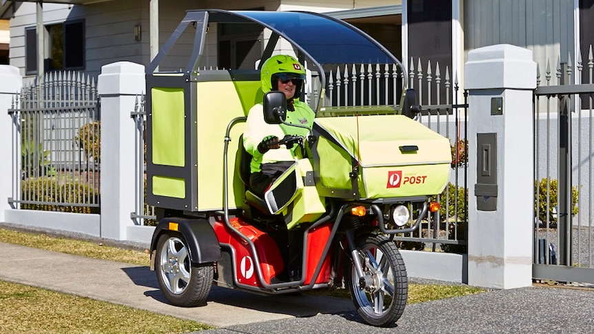 A postie clad in fluro yellow clothes rides a motorised three wheeled motorbike which has a sunshade over the top.