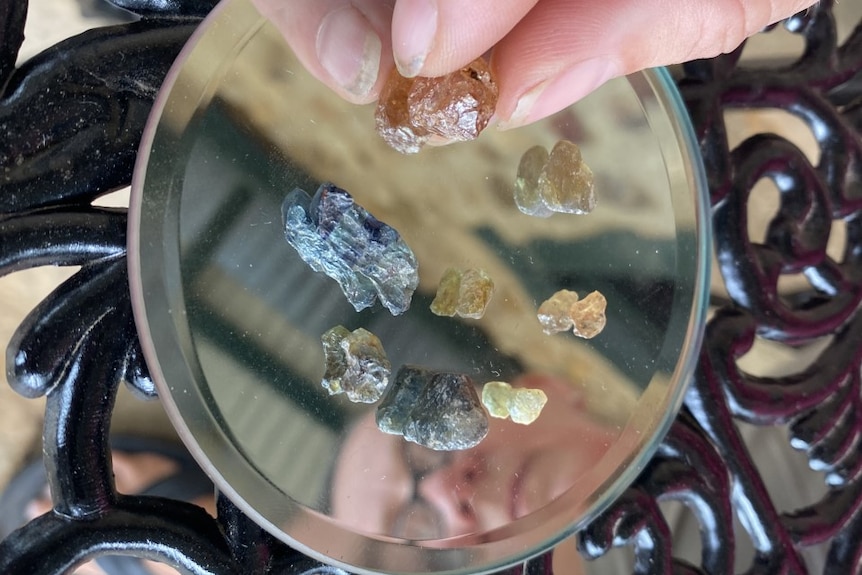 Six gemstones on a mirror with woman's face reflecting.