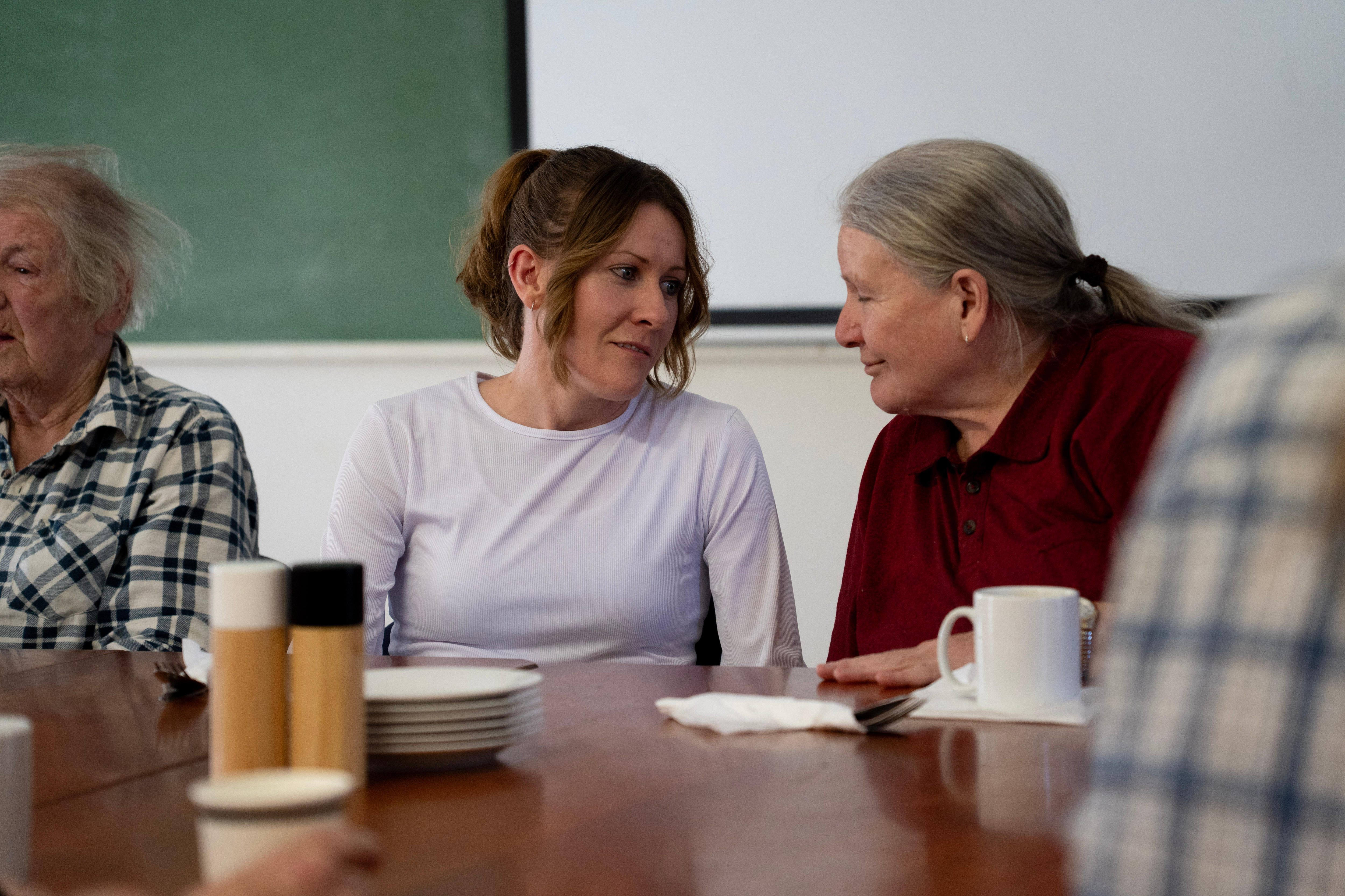Duas mulheres sentadas à mesa sorrindo uma para a outra
