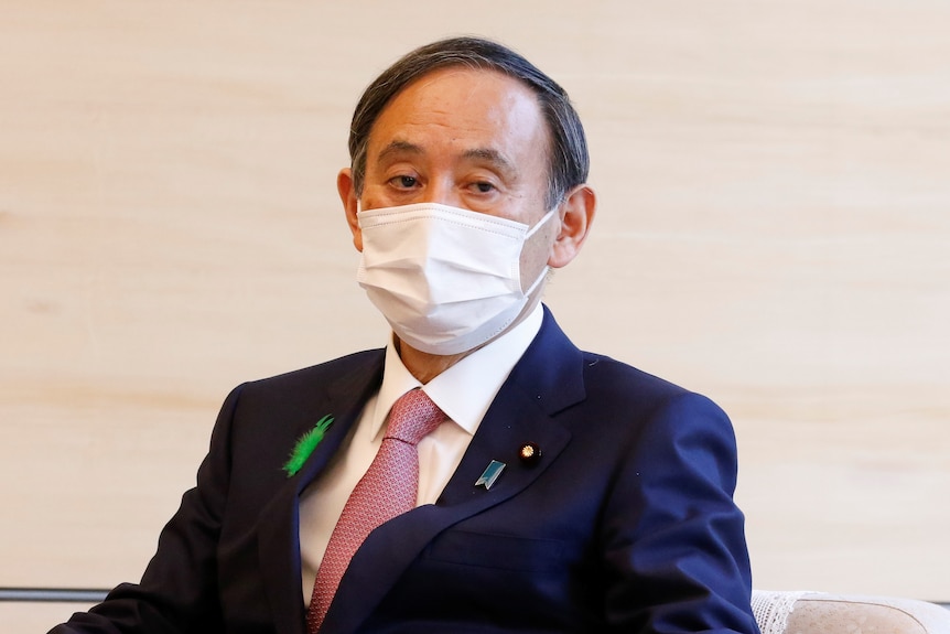 Yoshihide Suga wearing a suit and tie, with a white face mask over his mouth 