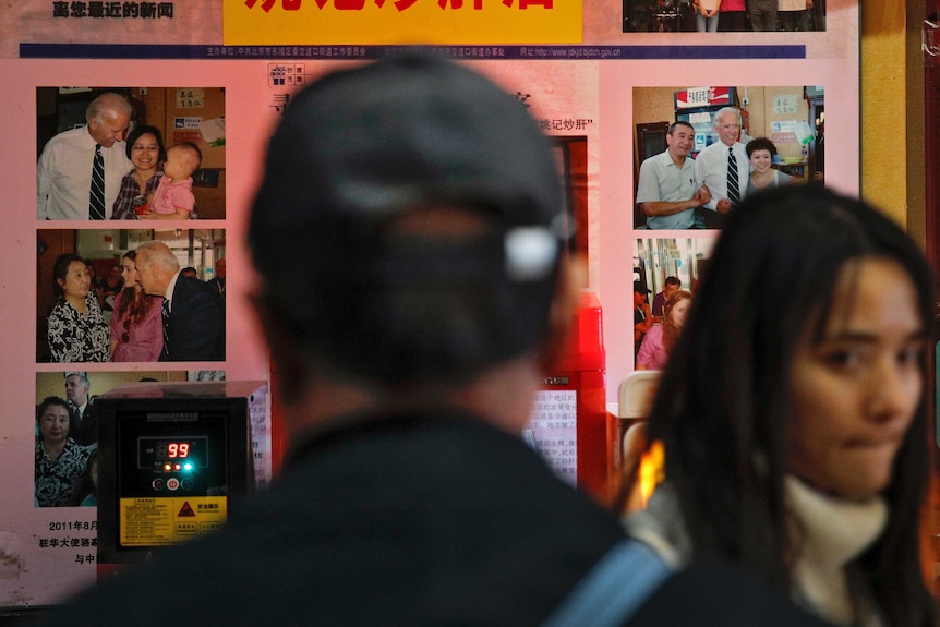 A man looks a screen with Joe Biden pictures while a woman walks by