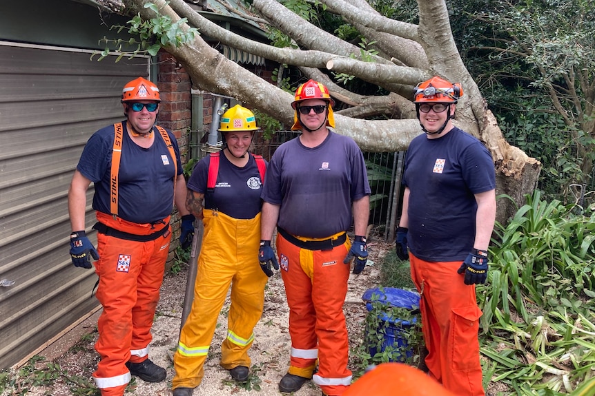 Four Victorian SES members, three men and a woman, standing outside a storm-damaged house