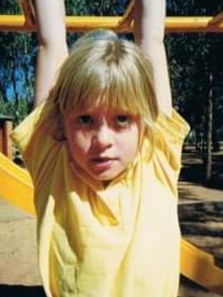 A blonde haired schoolgirl hangs from monkey bars