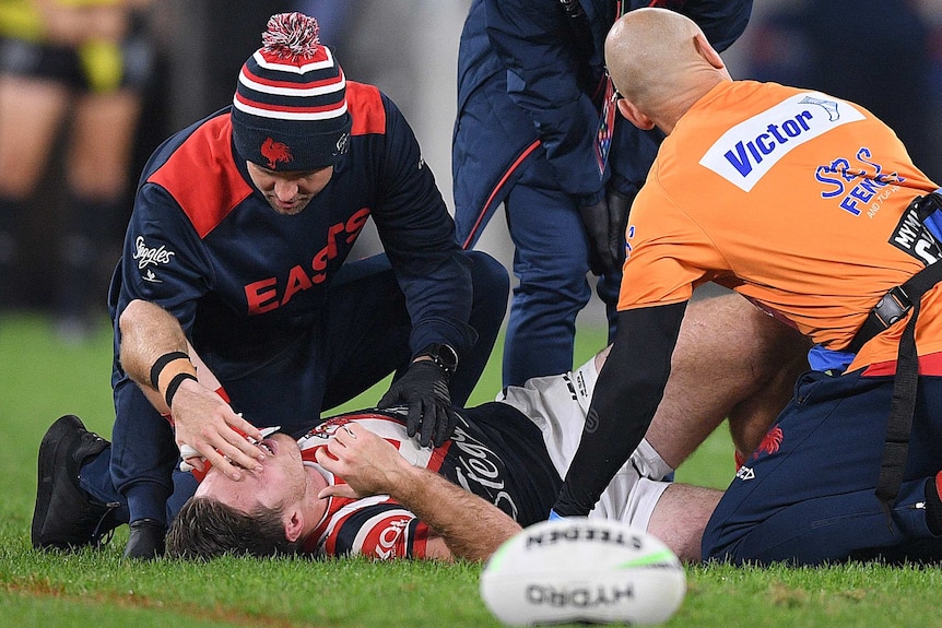 A Sydney Roosters NRL player holds his face as he receives treatment for a knee injury against St George Illawarra.