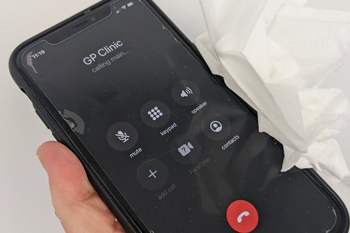 A mobile phone calling 'GP clinic' being held with a wad of tissues