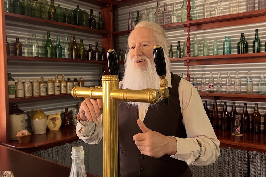 A wax doll of a man with long white hair and beard behind a bar
