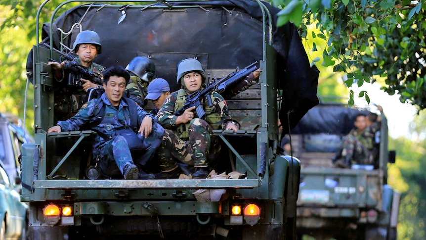 Filipino government soldiers with machine guns and green and blue army fatigues ride in the back of a vehicle near Marawi city.