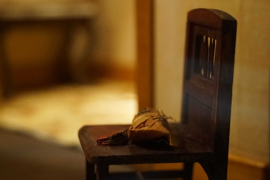 A tiny crime scene — a model of a chair with wrapped meat and a purse on it.