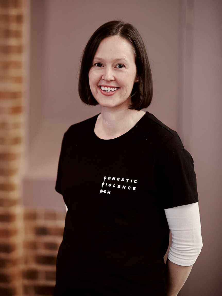A woman with shoulder-length brown hair and a black tshirt smiles towards the camera