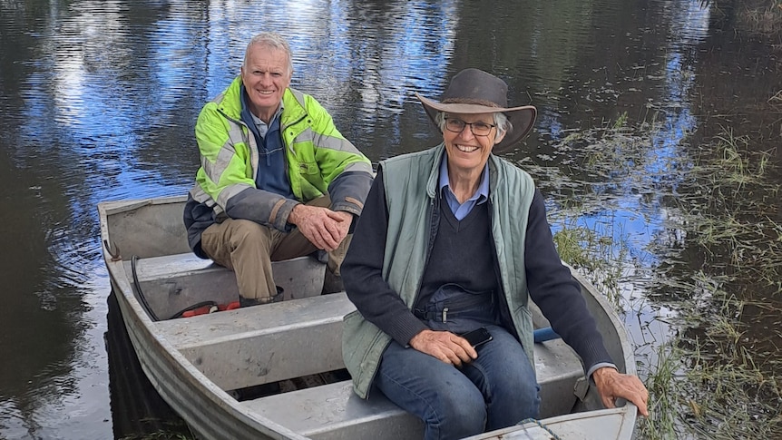 Two people sit in a boat in floodwaters.