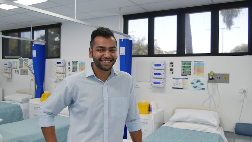 A man wearing a blue shirt in front of hospital beds