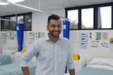 A man wearing a blue shirt in front of hospital beds