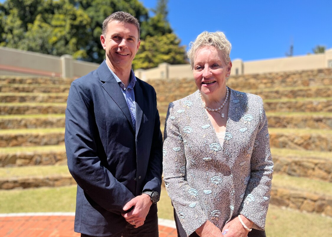 midshot of man and woman in suit jackets smile at camera